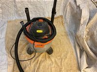 Overall view of the Ridgid wet/dry vacuum with hoses wrapped around and placed on a beige cloth background.