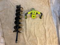 Metal auger bit and brushless motor handle assembly laid flat on beige cloth