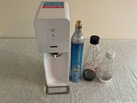Front view of white Sodastream machine, CO2 cylinder, and three plastic bottles