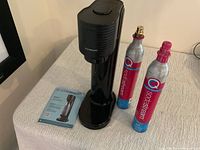 Front view of the black SodaStream Gaia sparkling water maker with instruction manual, and two CO2 cylinders.