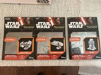 Three Metal Earth Star Wars metal model kits, including Darth Vader's X1 Starfighter, Millennium Falcon, and an opened R2-D2 model kit, shown in package.