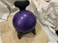 Purple yoga ball mounted on a black plastic chair base with caster wheels, shown from front with backrest.