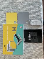 Image showing the ViewSonic M1 Mini original box with an image of the projector, two interchangeable top plates in yellow and grey, a remote control, and a product manual.
