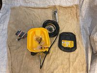 Overhead view of sprayer base unit, spray gun, hose, lid, manual and accessory bag on drop cloth