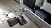 Several baking pans and dishes arranged on floor, including glass square and round dishes, metal round cake pan, and rectangular pans, plus muffin tin.