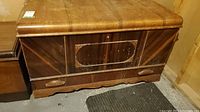 Closed view of the antique chest showing wood grain pattern, decorative front panel, bottom drawer with handles.