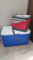 Photo showing the large blue cooler with white lid and the red Thermos soft-sided cooler placed on top, highlighting overall size and colors.