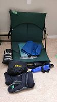 ThermaRestR chair with back support, blue cloth, black waterproof bags on carpeted floor with camp pillow pouch and water shoes