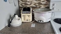Three kitchen appliances including T-fal Avante Deluxe two-slice toaster, Rival Crock-Pot slow cooker, and Toastess electric kettle on countertop.