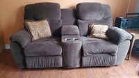 Front view of gray fabric recliner sofa with two pillows and center console with cup holders.