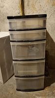 Five drawer plastic storage bin, tall with black top and black lining on drawers, located in basement.