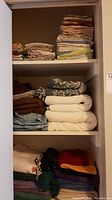 Shelves with folded bath towels, hand towels, face cloths, sheets and a throw in various colors and patterns organized in stacks.