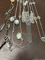 Seven silver-toned long necklaces and a pair of Austrian crystal earrings laid out showcasing various pendant styles including filigree tassels, key charm with crystals, and opalescent oval crystal. Accessories appear gently used and in good condition.