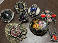 Photo showing 7 assorted assorted brooch pins including crystal, hand-painted wood, and metal pieces