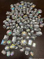 Top-down photo of mixed acrylic flat-back crystals with iridescent reflective surfaces spread on a dark surface.