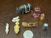 Top view of all miniatures arranged showing glass teapot and perfume bottle, metal elephant and sleigh, plastic figures, chess knight, thimble and small animal figurines with dime for scale