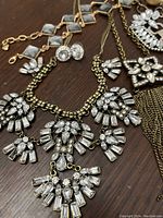 Close-up of crystal necklace featuring rectangular and round crystals on antiqued gold chain, alongside matching stud earrings and bracelets