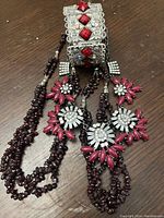 Image of two multi-strand garnet beaded necklaces with flower embellishments and the metal glass cuff.