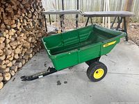 Full side view of green poly utility cart attached to black steel hitch, yellow wheel visible
