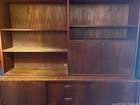 Front view of two-piece wooden wall unit showing shelved left section, right side drop-down door, sliding doors and drawers below.