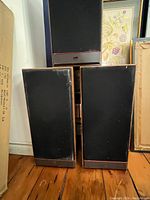 Front view of 3 large PSB speakers, showing wood veneer cabinets and black fabric covers, some wear visible