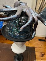 Front side view of black felt top hat with large hand-painted rubber Cthulhu figure mounted on the crown, showing studded bead decoration on the hat.