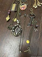 Two one-of-a-kind talisman necklaces with large decorative keys, Nevermore raven pendant necklace, distant view of faux pearl chandelier earrings, crystal pendant and earrings, metal snake bangle on wooden surface.