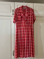 Full view of the coral and white checkered dress hanging on a hanger against white cabinets