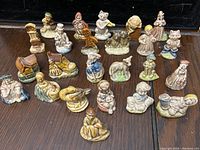 Front view of all 23 Wade Nursery Rhyme ceramic figurines arranged side by side on a dark surface showing a variety of characters including animals and children in pastel colors.