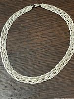 Full view of the wide braid sterling silver necklace laid flat on wood surface, showing its full length and lobster claw clasp.