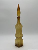 Full view of amber-colored Empoli glass decanter with stopper against plain background.