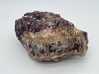 Amethyst boulder displaying purple crystal clusters and natural matrix from one side.