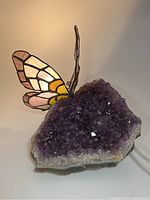Amethyst geode lamp with stained glass butterfly wings illuminated by LED bulb, cord visible.