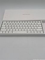 Front view of Apple Wireless Keyboard Model A1644 inside its box showing white keys and aluminum body.
