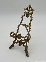 Front angled view of brass easel highlighting ornamental floral and scroll design.