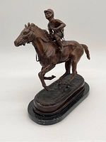 Solid bronze racehorse sculpture with jockey on top, mounted on a speckled black marble base, side angle view showing detailed features of horse and rider.