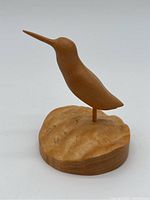 Front angle of carved wooden hummingbird on textured wooden base, showing smooth carving and natural wood grain.