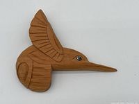 Front view of carved cedar hummingbird showing detailed wing and abalone eye inlay.