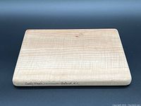 Rectangular figured maple cutting board with smooth rounded edges and inscription on side