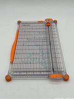 Top view of the Fiskars cutting tool showing clear plastic base with grid lines, orange blade slider, and orange handle on side.