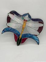 Front view of stained glass dragonfly with multicolor glass segments, wire hanger visible on top.