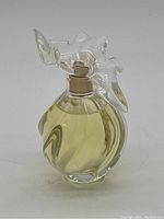 Front angle view of the Lalique glass perfume bottle filled with pale yellow perfume liquid, showcasing sculpted glass dove cap and rounded bottle shape.
