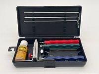 Open black plastic Lansky sharpening kit case showing contents including honing oil, sharpening stones, three sharpening rods and clamp system.