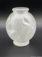 Front angle of frosted glass vase showing rounded form and embossed floral relief of water lilies and leaves.