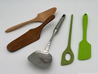 Photo showing two solid wood servers, one stainless steel spatula with Henckels logo, and two green plastic utensils (spatula and slotted spoon).