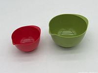 Two small Rosti Mepal mixing bowls in red and green, showing front and top side, illustrating size difference and shape.