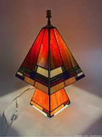 Stained glass pyramid lamp turned on showing orange and red tones illuminating