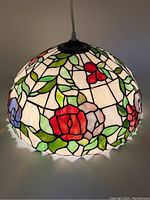 Lit view of 16 inch diameter stained glass pendant lamp showing colorful floral pattern with red, blue, and pink flowers and green leaves on white background