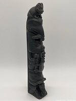 Angled full-length view of the carved totem pole showing overall shape and stacked figures