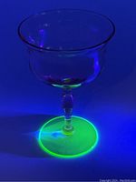 Uranium glass goblet glowing under UV light showing bright green fluorescence on the base and stem.